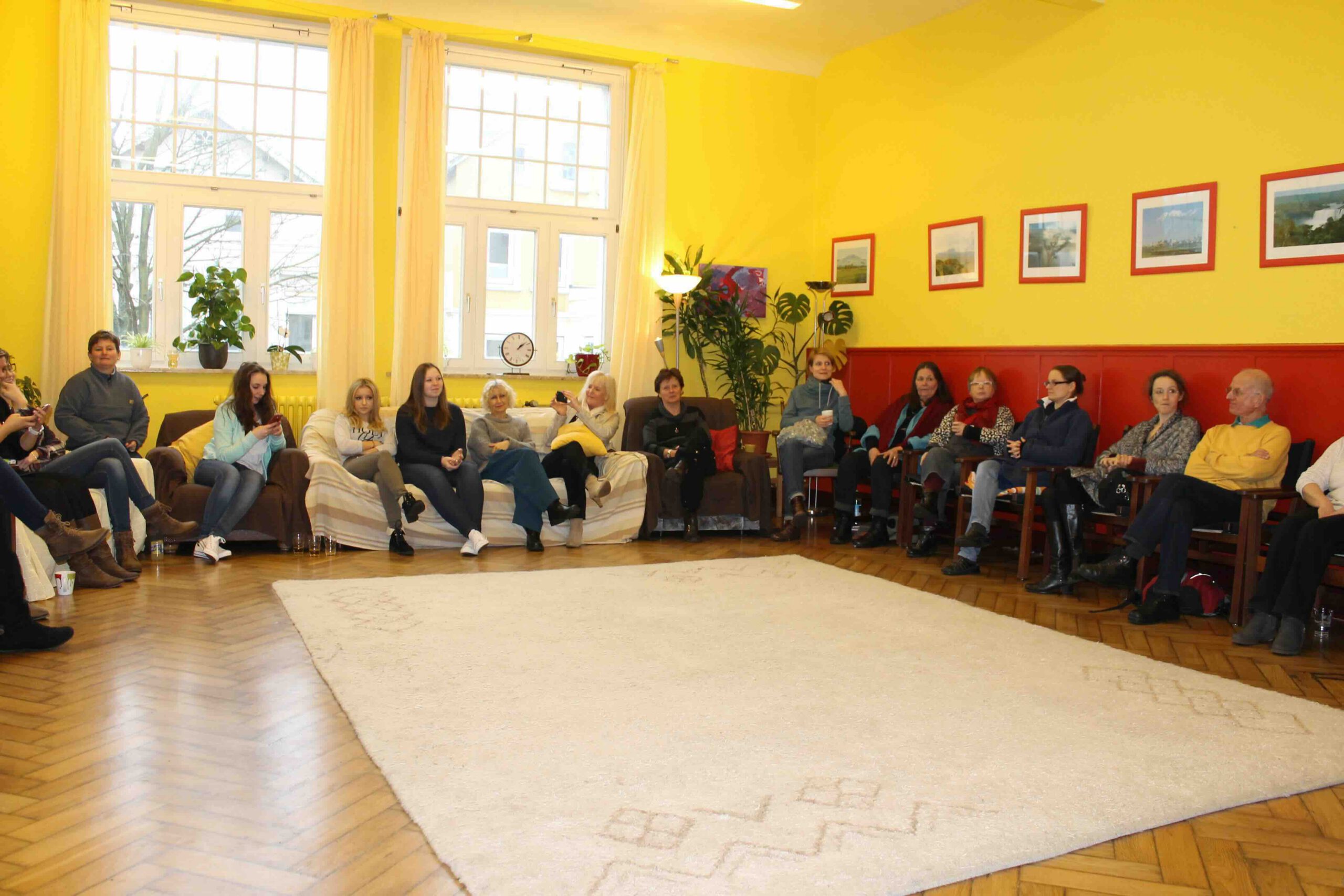 Teilnehmer einer Gruppenfortbildung im MVZ Timmermann und Partner sitzen in einem Stuhlkreis in einem hellen Seminarraum mit gelben Wänden.