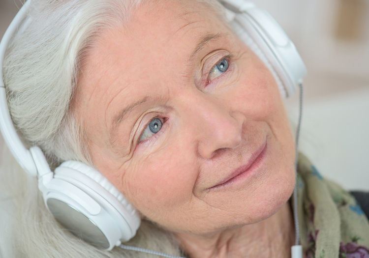 Ältere Frau mit Kopfhörern, die Musik hört und dabei entspannt wirkt – Symbol für den Einsatz von Musiktherapie bei Demenz.