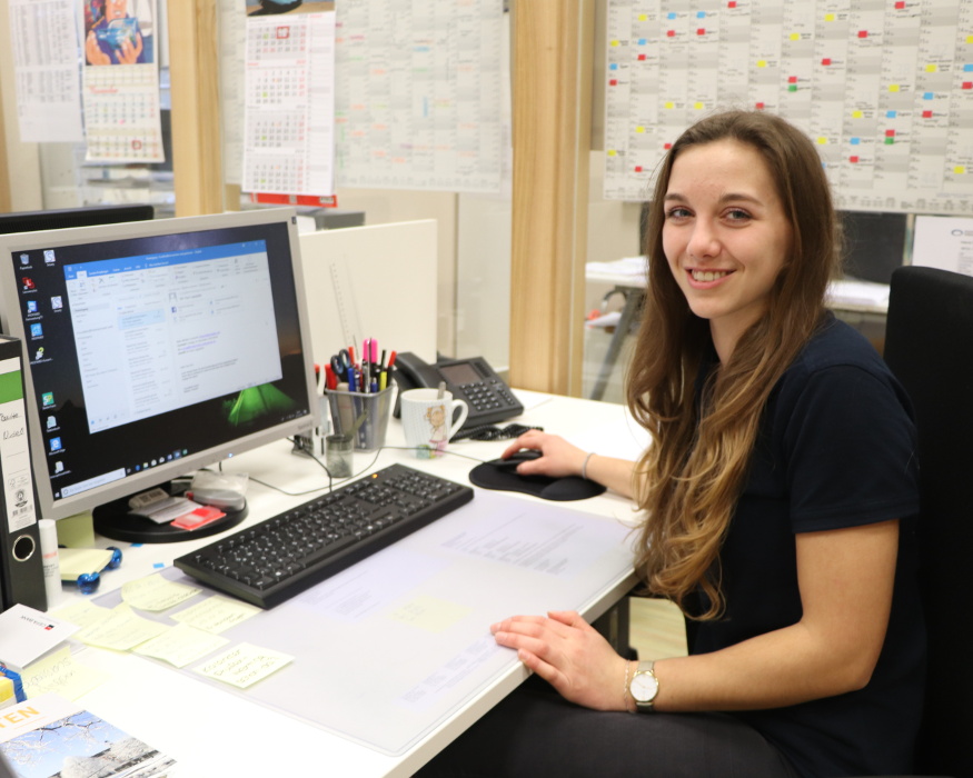 Junge Frau sitzt am Schreibtisch vor dem Computer und lächelt – erfolgreiche Teilnehmerin des Azubi-Speeddatings in Cuxhaven.