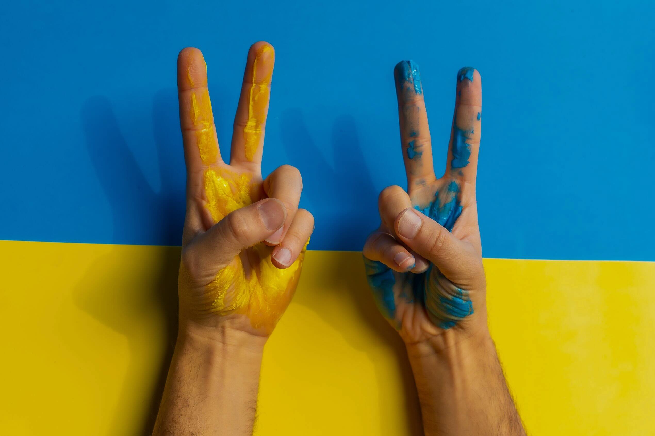 Zwei Hände mit gelber und blauer Farbe in den Farben der ukrainischen Flagge zeigen das Peace-Zeichen.
