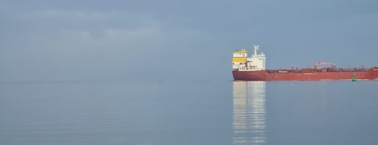 Ein großes rotes Frachtschiff fährt ruhig auf der Nordsee, der Himmel ist leicht bewölkt.