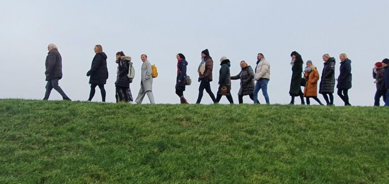 Mitarbeiter*innen des MVZ Timmermann und Partner spazieren bei sonnigem Wetter auf dem Deich während des Begrüßungstags im Februar 2023.