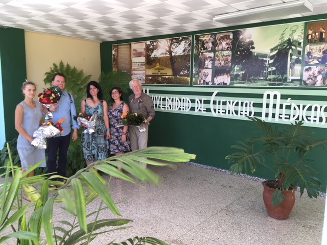 Gruppe von Fachleuten, darunter Jochen Timmermann, Maria Hurtado und Carolin Baucke, mit Blumen vor der Universidad de Ciencias Médicas in Santiago de Cuba beim Kongress für Psychosomatische Medizin.