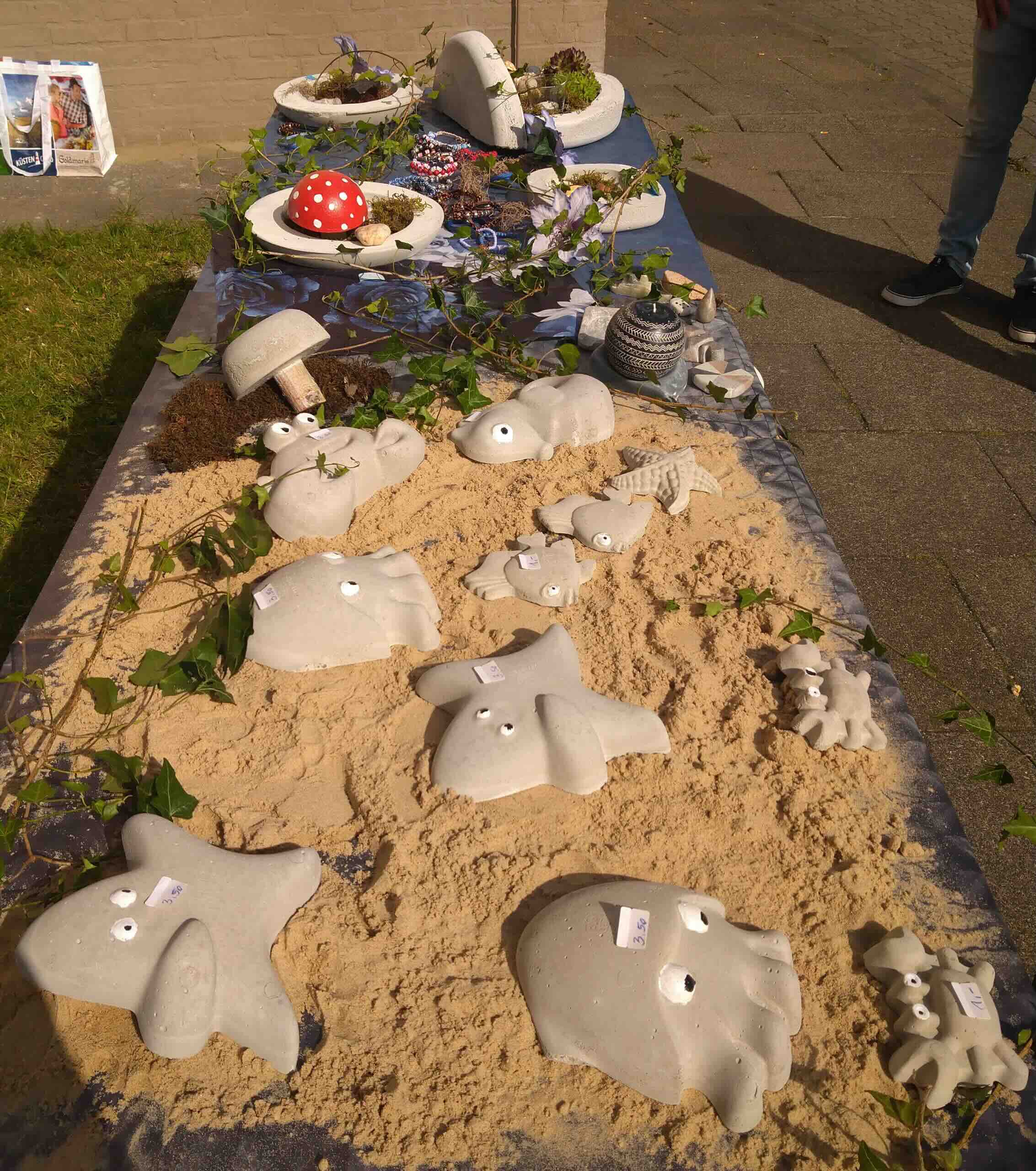 Ergotherapeutische Projektarbeiten der Tagesgruppe des MVZ Timmermann und Partner – Figuren aus Beton, Speckstein und Armbänder auf einem Verkaufstisch.