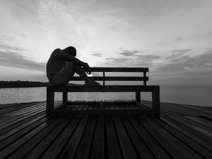 Schwarz-weiß Foto eines nachdenklichen Mannes, der allein auf einer Bank am Wasser sitzt – Symbolbild für Suizidgedanken, Einsamkeit und Tabuthemen.